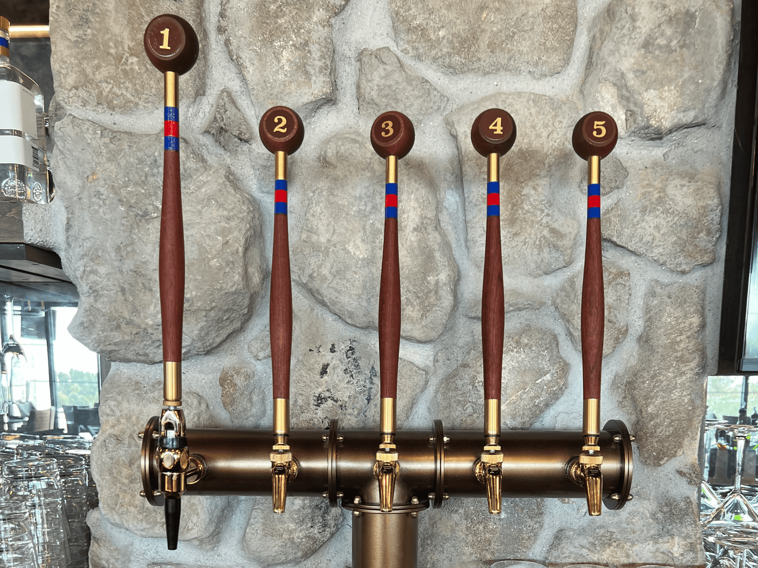 Five draft beer taps with numbered handles in a brewery setting.